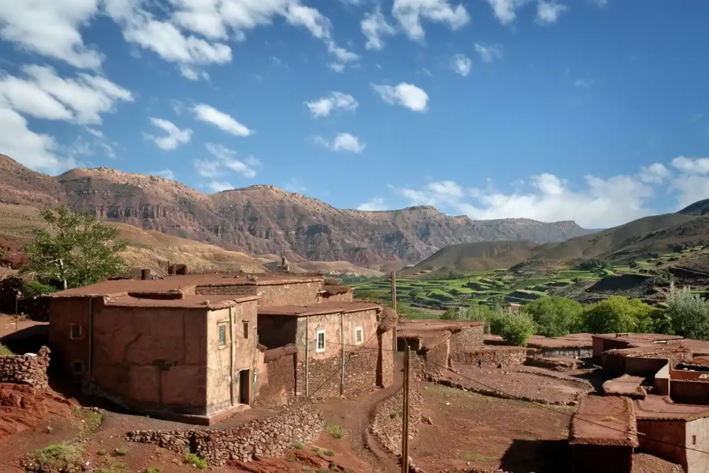 Traditional red clay village nestled in the Atlas Mountains of Morocco with terraced green fields.