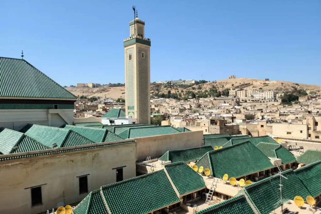 Green tiled roofs and a tall minaret overlook the ancient Fes Medina in Morocco.

